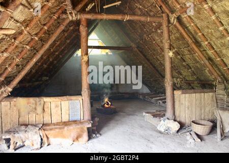 Butser Ancient Farm - Internal view of neolithic house with open fire, animal hides and sleeping areas. Stock Photo