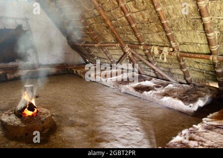 Butser Ancient Farm - Internal view of neolithic house with open fire, animal hides and sleeping areas. Stock Photo