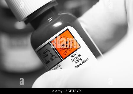 Toxic warning label on a plastic chemical bottle being held by a person wearing gloves. Selective colour image Stock Photo