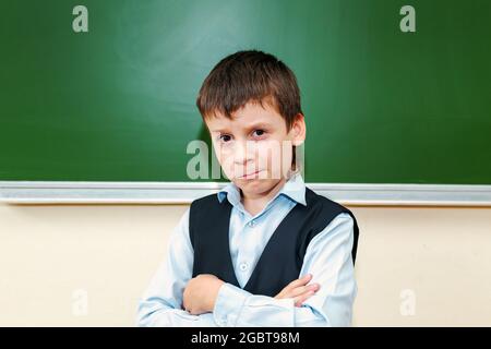 Funny schoolboy near the green school board in the classroom. Elementary school child. Back to school. Stock Photo