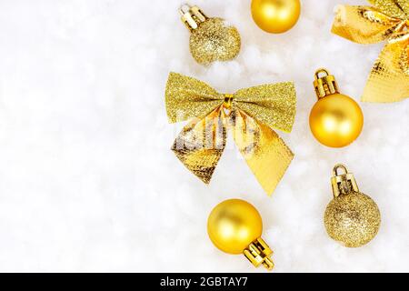 Bright golden and yellow Christmas decorations (ribbons, baubles, ornament) flat lay on white artificial snow background with copy space. Christmas an Stock Photo