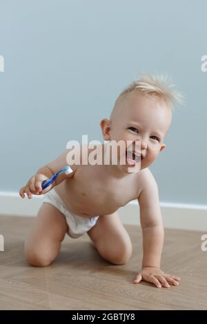 little boy brushes his teeth with a toothbrush and laughs, against the background of a blue wall Stock Photo