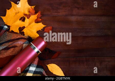 Autumn flat lay. Thermos with hot coffee, plaid and fallen leaves on a wooden background. Beginning of the fall season. Copy space. Stock Photo