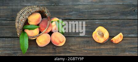 Ripe juicy peaches with green leaves next to a wicker basket on an old rustic table. Concept of growing your own organic food. Stock Photo