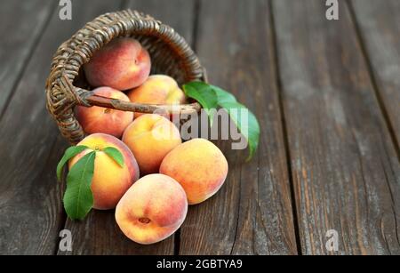 Fresh juicy ripe peaches in a inverted wicker basket on an old wooden table, selective focus at the bottom of the image. Healthy eating concept. Stock Photo