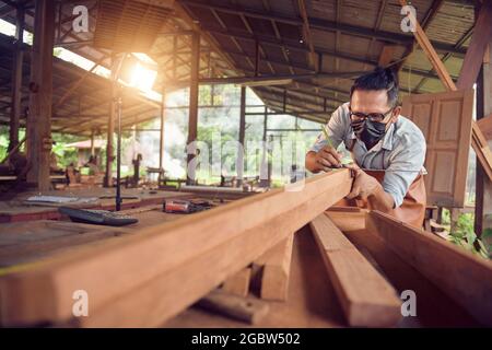 professional carpenter holding a angular ruler and pencil while measuring a board in a carpentry workshop,vintage style Stock Photo