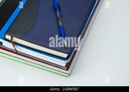 stack of notebooks and diaries with a blue pen on the top on a white background Stock Photo