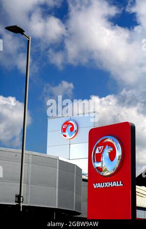 Vauxhall's griffin logo at a car dealership seen against a background of blue sky and clouds. Stock Photo