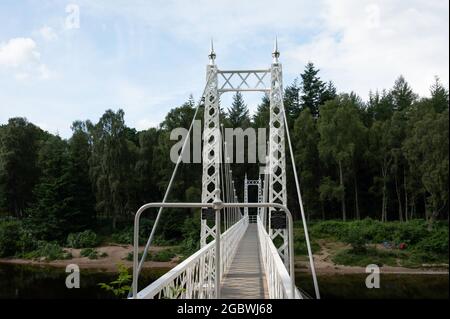 The white Cambus O'May suspension bridge over the River Dee with forest, blue sky and clouds in background. Stock Photo