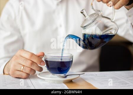 A man in a white shirt pours blue Chinese tea from a transparent teapot into a mug Stock Photo