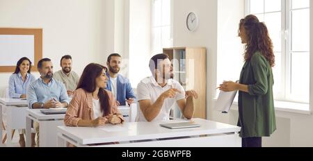 Coach having discussion with group of happy people who are sitting at desks in classroom Stock Photo