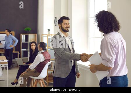 Two happy businessmen or office coworkers shake hands as they meet in a business meeting Stock Photo