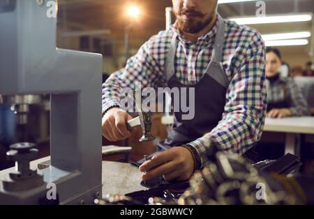 Footwear factory worker sitting at table and using professional tools to make new leather boots Stock Photo