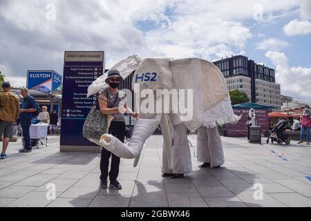 London, UK. 05th Aug, 2021. Demonstrators wearing an 'HS2' white elephant costume are led outside the train station by a fellow demonstrator during the Stop HS2 protest.Activists gathered outside King's Cross Station in protest against the new High Speed 2 (HS2) railway system, which environmentalists say will be 'ecologically devastating' and will cost taxpayers £170 billion. (Photo by Vuk Valcic/SOPA Images/Sipa USA) Credit: Sipa USA/Alamy Live News Stock Photo