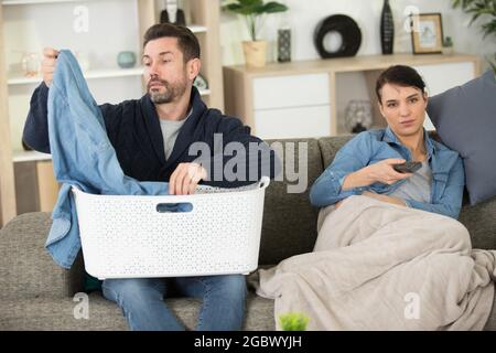 man doing laundry while woman is watching tv Stock Photo