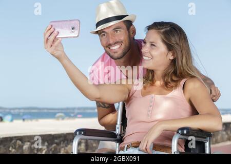 couple in wheelchair in love taking selfies outdoors Stock Photo