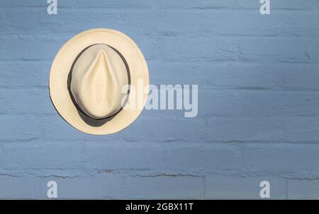 Single Panama Straw Hat Hanging Against A Blue Painted Brick Wall, England UK Stock Photo