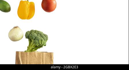 Isolated on white background levitating vegetables tomato, pepper, avocado, onion, broccoli over a paper bag for shopping. Delivery service concept. Stock Photo