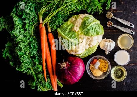 Curried Cauliflower Rice Kale Soup Ingredients on a Wood Table: Cauliflower with other vegetables and spices on a dark wooden background Stock Photo