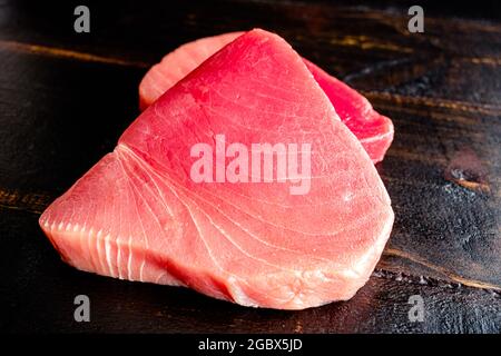 Raw Tuna Steaks on a Dark Wood Background: Closeup view of uncooked tuna steaks on a wooden table Stock Photo
