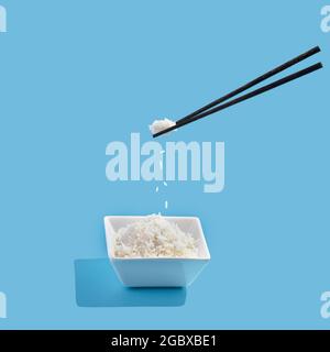 ceramic bowl with rice and levitation chopsticks on a blue background. Stock Photo
