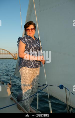 A luxurious yacht vacation. Happy pretty middle-aged woman in sunglasses on the boat deck floats on the river. Stock Photo