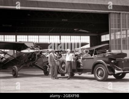 1920s 1930s COUPLE WITH CONVERTIBLE PACKARD CAR TALKING TO AIRPLANE SALESMAN AT HANGAR  - a9229 HAR001 HARS COMMUNICATION VEHICLE INFORMATION LIFESTYLE PLANES FEMALES MARRIED SPOUSE HUSBANDS LUXURY COPY SPACE FULL-LENGTH LADIES PERSONS AUTOMOBILE MALES TRANSPORTATION MIDDLE-AGED B&W PARTNER MIDDLE-AGED MAN GOALS SELLING PROPELLER ADVENTURE AIRPLANES CUSTOMER SERVICE AUTOS EXTERIOR RECREATION OPPORTUNITY AVIATION OCCUPATIONS PURCHASE AUTOMOBILES STYLISH VEHICLES HANGAR AIRFIELD COOPERATION MID-ADULT MID-ADULT MAN MID-ADULT WOMAN PACKARD SALESMEN WIVES BLACK AND WHITE CAUCASIAN ETHNICITY Stock Photo
