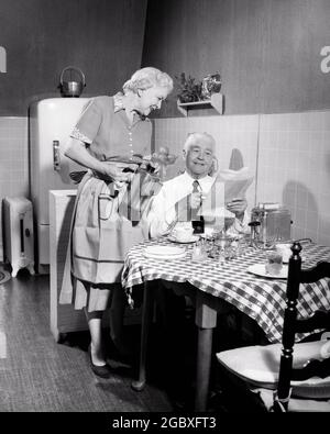 1950s ELDERLY SENIOR RETIRED COUPLE AT APARTMENT KITCHEN TABLE HAVING BREAKFAST WOMAN POURING COFFEE FOR MAN READING NEWSPAPER  - d366 HAR001 HARS HAVING COMMUNICATION TOASTER INFORMATION STRONG LIFESTYLE SATISFACTION ELDER FEMALES MARRIED SPOUSE HUSBANDS HEALTHINESS HOME LIFE COPY SPACE FRIENDSHIP HALF-LENGTH LADIES PERSONS CARING MALES SENIOR MAN SENIOR ADULT APARTMENT B&W PARTNER SENIOR WOMAN HAPPINESS OLD AGE POUR OLDSTERS HIGH ANGLE OLDSTER IN ELDERS CONNECTION PERSONAL ATTACHMENT AFFECTION EMOTION TOGETHERNESS WIVES BLACK AND WHITE CAUCASIAN ETHNICITY HAR001 OLD FASHIONED PERCOLATOR Stock Photo