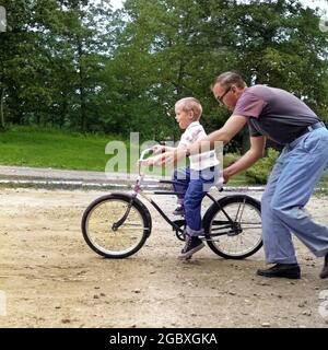 1960s MAN FATHER GIVING BOY SON ON BIKE A PUSH TEACHING HIM HOW TO RIDE BICYCLE - j11754c HAR001 HARS GIVING PUSH JUVENILE FEAR BALANCE TEAMWORK RIDE SONS LIFESTYLE PARENTING STARTING BIKING GROWNUP HEALTHINESS HOME LIFE HORIZONTAL COPY SPACE PEOPLE CHILDREN FRIENDSHIP FULL-LENGTH PHYSICAL FITNESS PERSONS CARING MALES PEDAL CONFIDENCE BICYCLES TRANSPORTATION FATHERS PATERNAL BIKES SINGLE PARENT RELEASES SINGLE PARENTS FATHERHOOD HAPPINESS LEISURE AND CHALLENGE DADS EXCITEMENT HOW QUALITY TIME RECREATION DIRECTION QUALITY SUPPORT STEADYING GROWTH HIM JUVENILES MID-ADULT MID-ADULT MAN PARENTAL Stock Photo