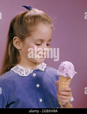 1960s LITTLE GIRL SMILING AS SHE LOOKS AT HER SWEET REFRESHING STRAWBERRY ICE CREAM CONE - kf3695 HAR001 HARS TREAT HOME LIFE COPY SPACE HALF-LENGTH EXPRESSIONS HAPPINESS CHEERFUL CHOICE SHE SMILES JOYFUL LOOKS STYLISH ICE CREAM JUVENILES REFRESHING CAUCASIAN ETHNICITY HAR001 OLD FASHIONED Stock Photo