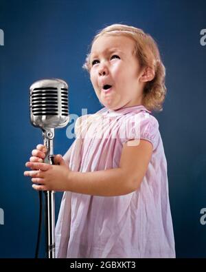 1940s LITTLE GIRL MAKING FACE SINGING INTO MICROPHONE - r13231c HAR001 HARS CUTE FACIAL COMMUNICATION BLOND SINGER COMPETITION FEMALES WINNING STUDIO SHOT PORTRAITS COPY SPACE HALF-LENGTH SPEAK SING ENTERTAINMENT PERFORMING PERFORMING ARTS HAPPINESS RADIOS PERFORMER AUDITION EXCITEMENT SONG VOICE VOCAL OCCUPATIONS LITTLE GIRL POISE CLOSE-UP PERFORM PLEASANT STARLET AGREEABLE CHARMING CHROME CLOSE UP COMPETITOR DEBUT GROWTH JUVENILES LOVABLE MIKE PLEASING YOUNGSTER ADORABLE APPEALING CAUCASIAN ETHNICITY COMPETE HAR001 OLD FASHIONED Stock Photo