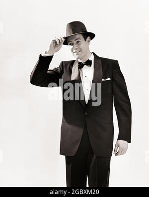 1950s MAN DRESSED IN TUXEDO TIPPING HIS HAT IN GREETING  - s1809 DEB001 HARS STYLES LOW ANGLE GESTURES SMILES INTRODUCTION JOYFUL STYLISH DEB001 FASHIONS MID-ADULT MID-ADULT MAN TIPPING BLACK AND WHITE CAUCASIAN ETHNICITY OLD FASHIONED Stock Photo