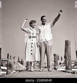 1940s 1950s YOUNG COUPLE WEARING STYLISH SUMMER CLOTHES STANDING ON WOODEN DOCK WAVING HELLO GOODBYE GOOD-BYE  - y745 HAR001 HARS NOSTALGIA OLD FASHION 1 GREETING STYLE COMMUNICATION YOUNG ADULT VACATION PLEASED JOY LIFESTYLE SATISFACTION FEMALES MARRIED SPOUSE HUSBANDS COPY SPACE FRIENDSHIP FULL-LENGTH LADIES PERSONS DOCK MALES CONFIDENCE B&W PARTNER TIME OFF HAPPINESS CHEERFUL ADVENTURE LEISURE HELLO TRIP GETAWAY LOW ANGLE RECREATION ON GOOD-BYE HOLIDAYS SMILES JOYFUL STYLISH TOGETHERNESS VACATIONS WIVES YOUNG ADULT MAN YOUNG ADULT WOMAN BLACK AND WHITE CASUAL CAUCASIAN ETHNICITY HAR001 Stock Photo