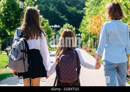 Two daughters in school uniform walking together with mother to school  Stock Photo