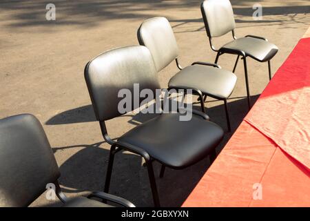 Black chairs on the street. Seats near the red table. Outdoor furniture. Places for participants. Stock Photo