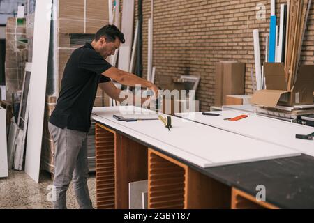 Man using a drill on a white surface in a workshop Stock Photo