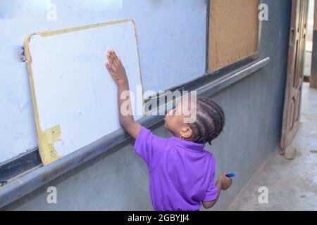 African girl child, pupil or student standing in a classroom and writing on a whiteboard while studying for excellence in her school, education Stock Photo