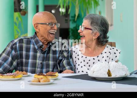 Elderly couple wearing glasses sitting at a table, both are smiling Stock Photo