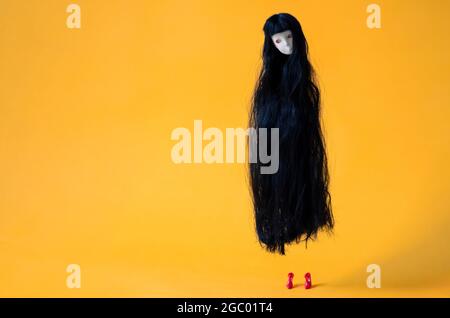 Long hair asian female ghost doll flying in the air with red high heel on the floor on orange background. Minimal Halloween scary concept. Stock Photo