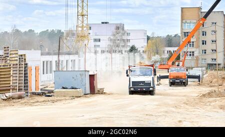 Grodno - April 2020: Crane and heavy lorry on construction site workplace with builders and machinery. Stock Photo