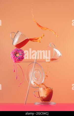 Tea and donut with pink glazing, balancing composition, action still life, splash photography Stock Photo