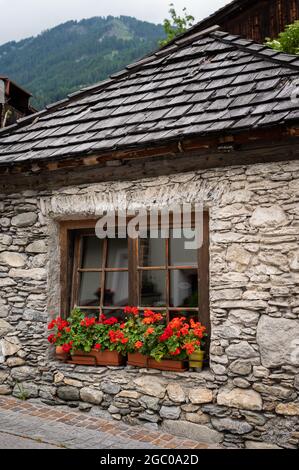 Old stone house with red flowers in Matrei in Osttirol, cloudy day in summer Stock Photo