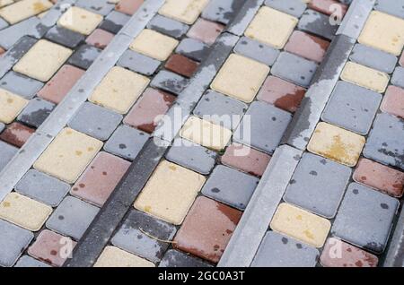 An angled view of the staircase from above, covered with multicolored paving tiles. Gray, yellow, red rectangular sidewalk blocks. Raindrops on the si Stock Photo