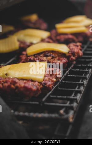 Burgers on the grill with gorm cheese melting on top of the meat. Meat cooked on the grill and charcoal. Heat on meat for cooking. Grilled meat for bu Stock Photo