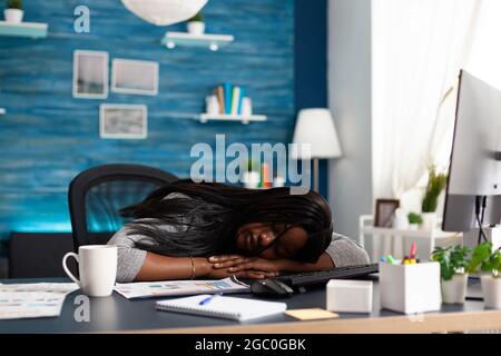 Exhausted tired workaholic black student sleeping on desk table in living room after working at deadline. Workaholic overworked disappointed african woman searching online business course Stock Photo
