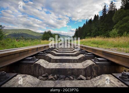 Railroad going into the distance Against Mountains And Beautiful Cloudy Sky, Near Forest. Landscape With Railway. Bottom view. Stock Photo