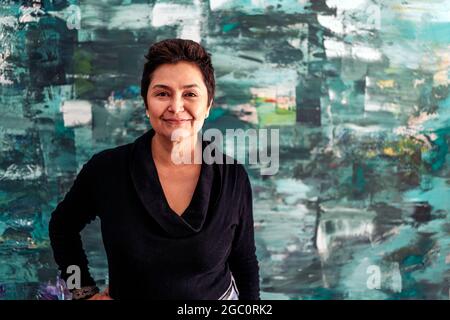 Cheerful middle aged woman smiling and looking at camera against her colorful artwork. Stock Photo