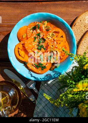 Yellow tomatoes salad with rye bread slices in blue ceramic bowl top view. Ripe fresh colorful vegetables mixed sliced greens with olive oil vinegar p Stock Photo