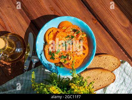Yellow tomatoes salad with rye bread slices in blue ceramic bowl top view. Ripe fresh colorful vegetables mixed sliced greens with olive oil vinegar p Stock Photo
