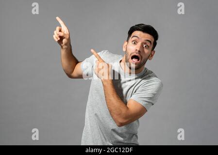 Shocked young Caucasian man with hands pointing up in isolated light gray studio background Stock Photo